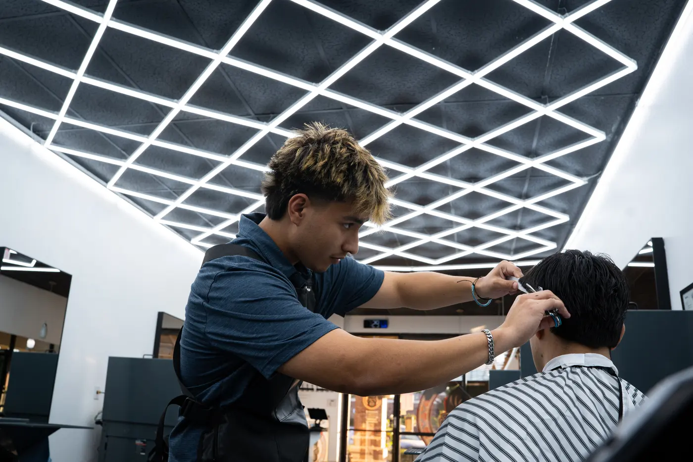 A barber cutting a customer's hair under shop lighting.